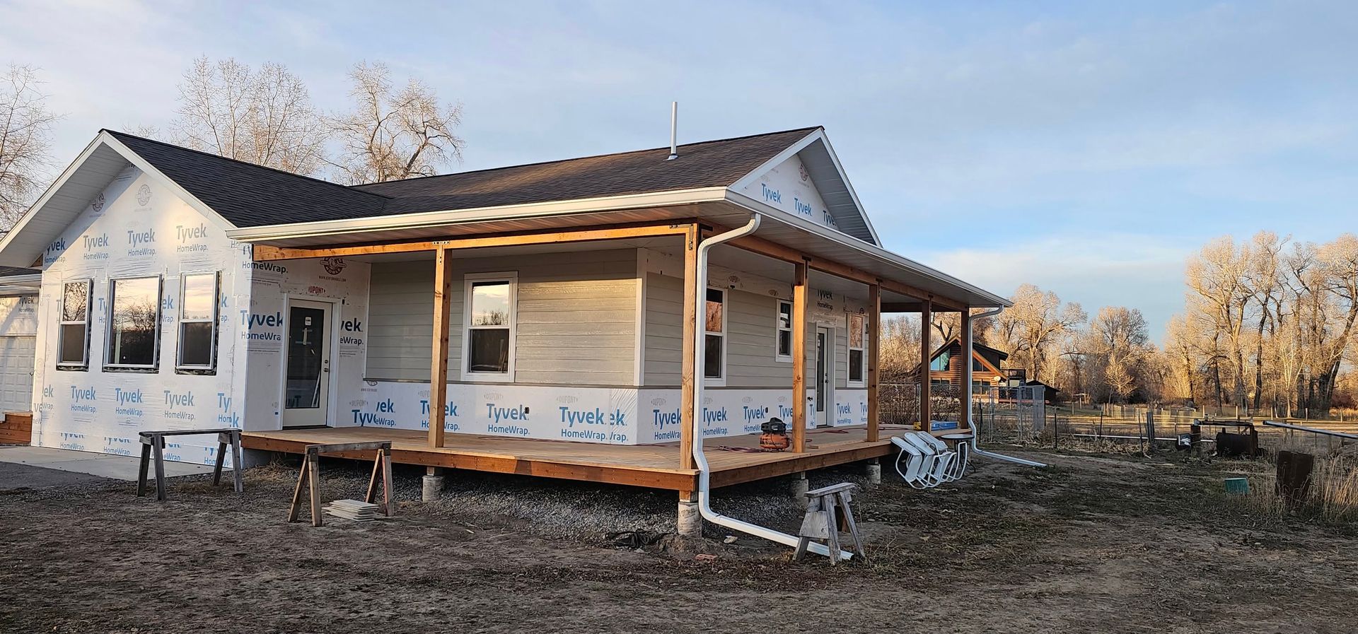 A single-story house under construction with white exterior sheathing and a wooden front porch in a rural, open landscape.