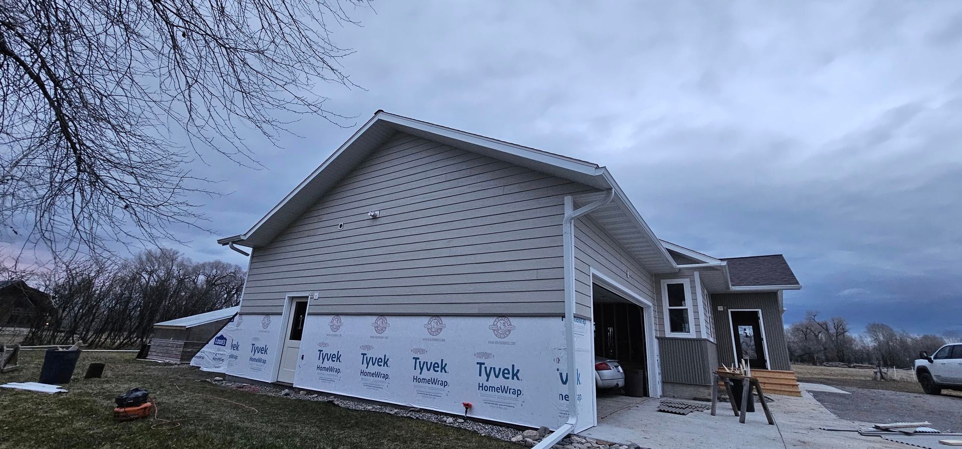 A house under construction with beige horizontal siding on the upper half and white protective house wrap on the lower half.