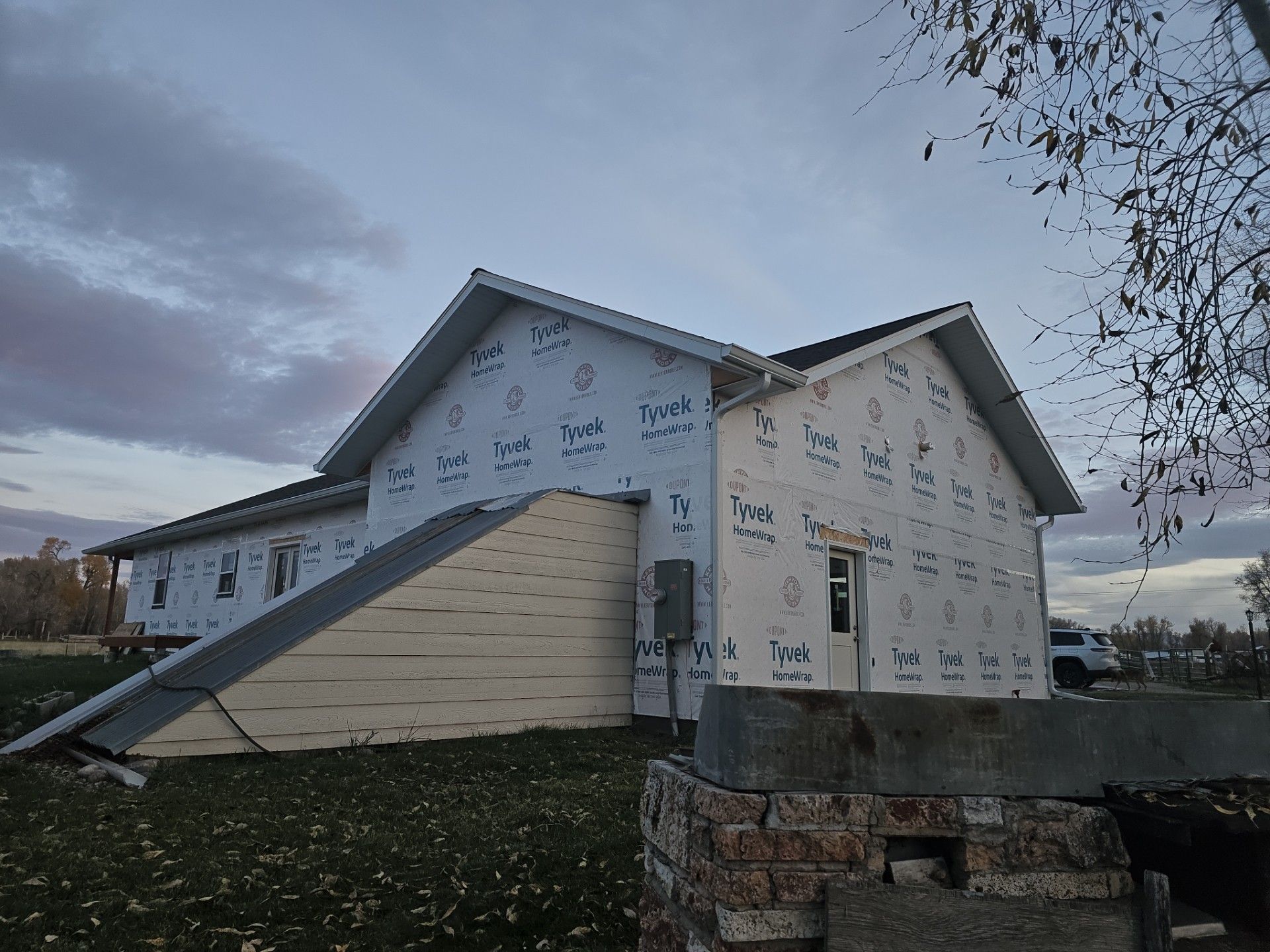A side view of a house under construction, featuring light-colored exterior sheathing and a protruding basement entrance.