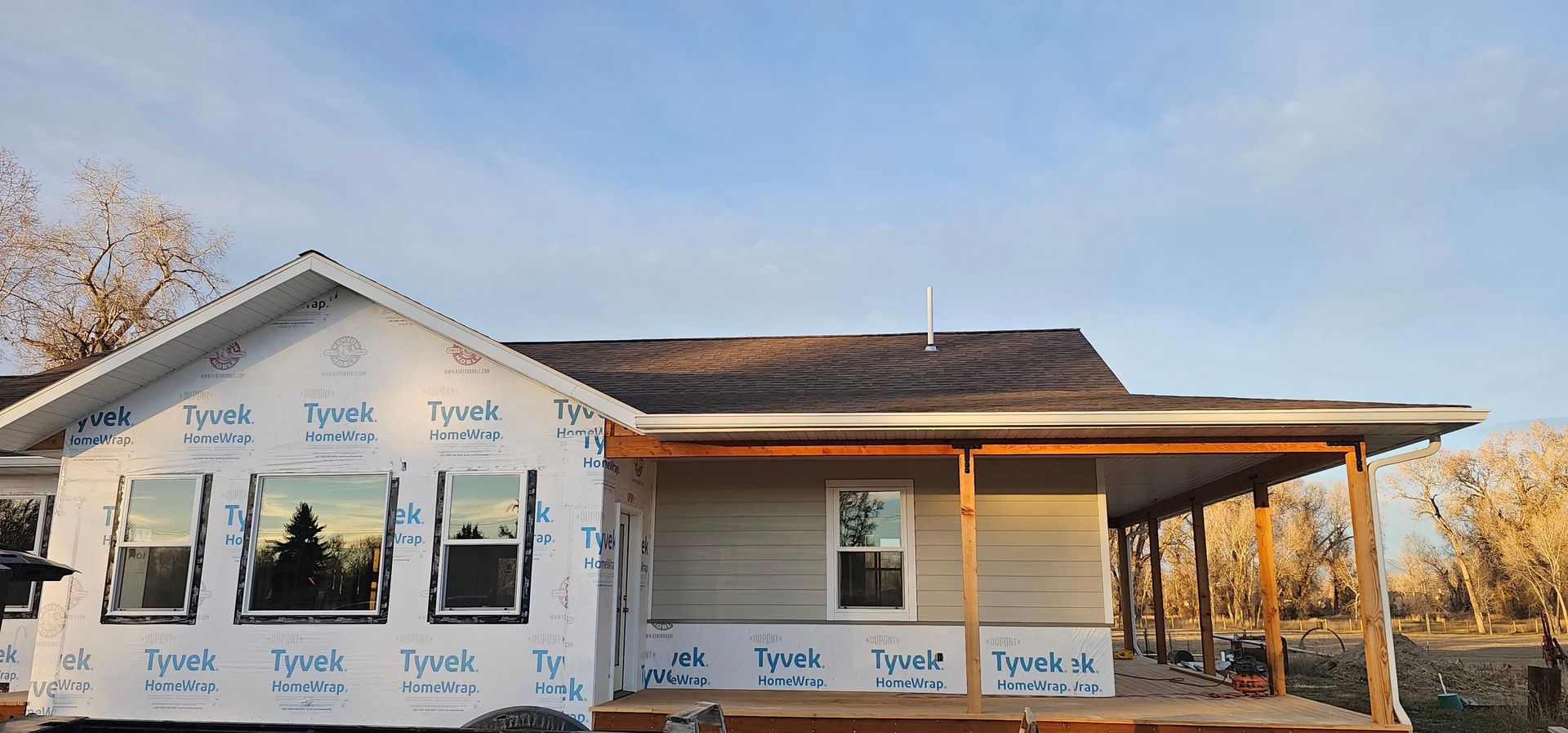 A house under construction with Tyvek-wrapped walls, installed windows, and an unfinished porch during the daytime.