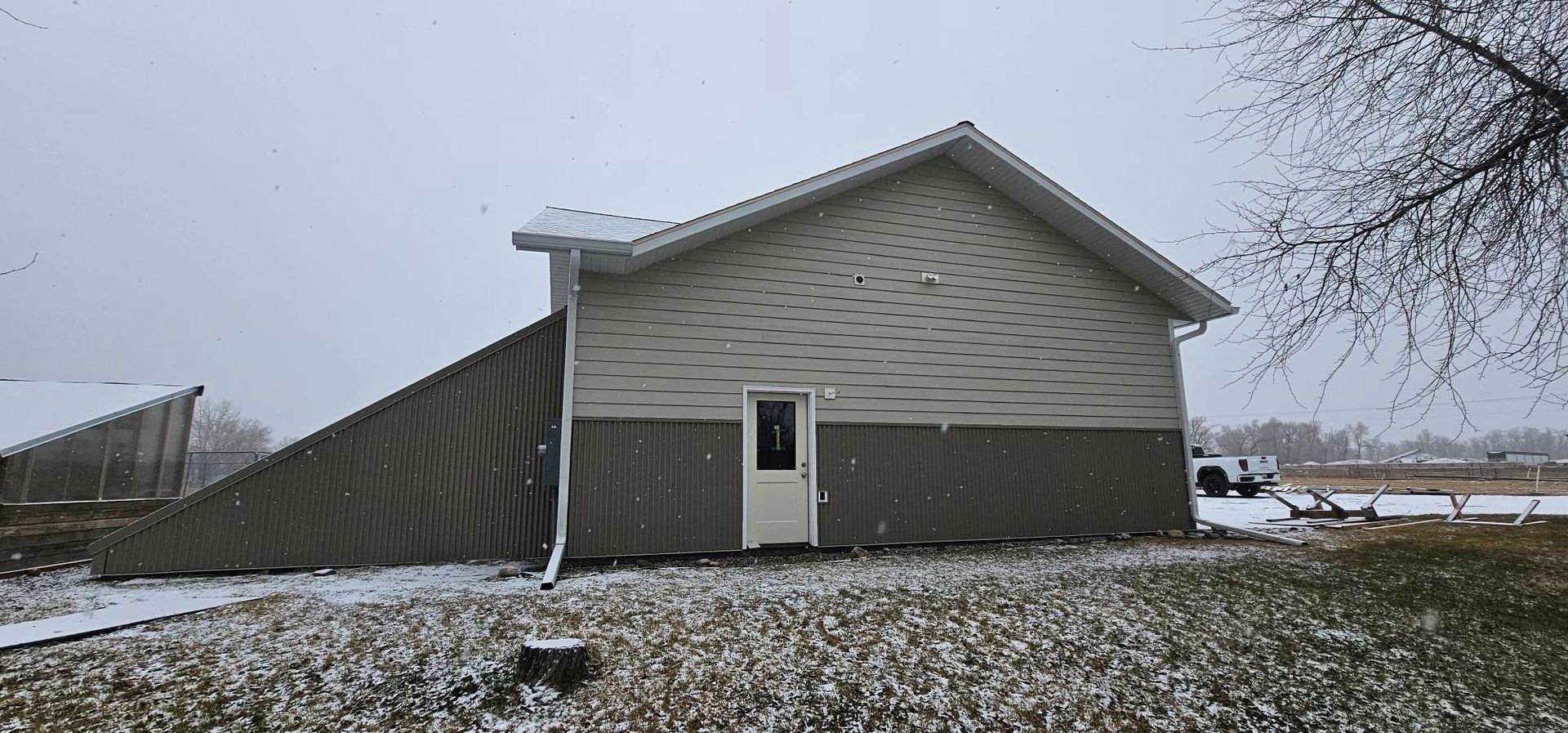 A beige and brown building exterior during a light snowfall, with a large, slanted brown tarp attached to one side.