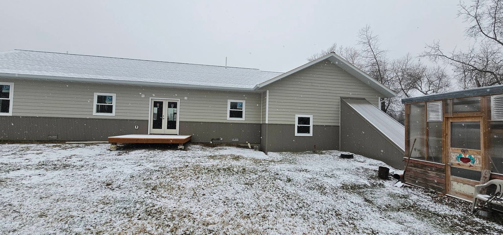 A beige, single-story house with a basement entrance and snow-covered yard, set against a cloudy, wintry sky.