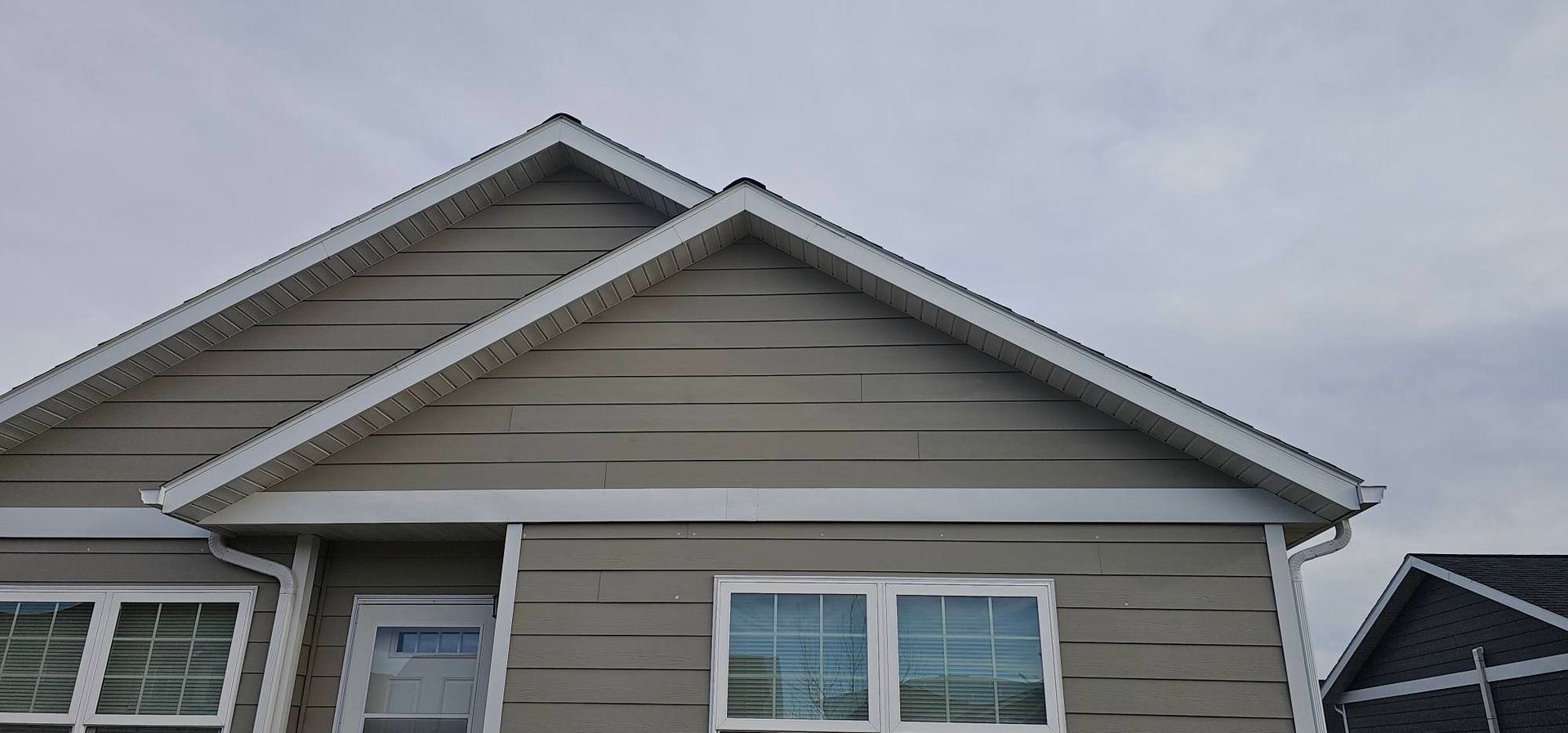 Gray vinyl siding on the side and gable of a house with white trim and windows under a cloudy sky.