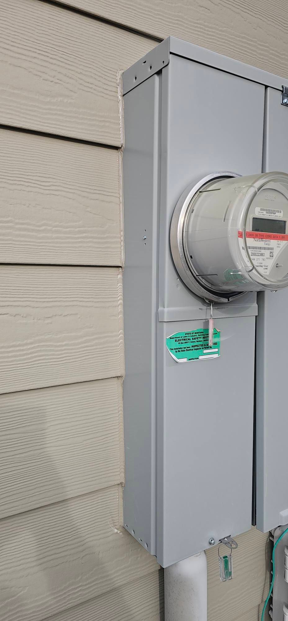 An electrical meter mounted on the side of a house with beige siding.