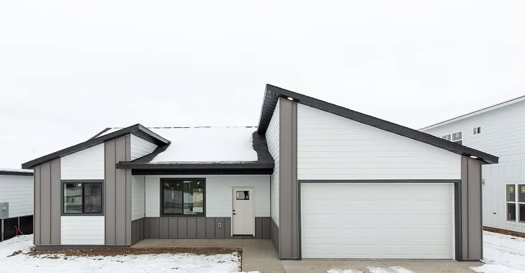 A single-story suburban house with white horizontal siding, gray vertical accents, a garage, and snow-covered ground.