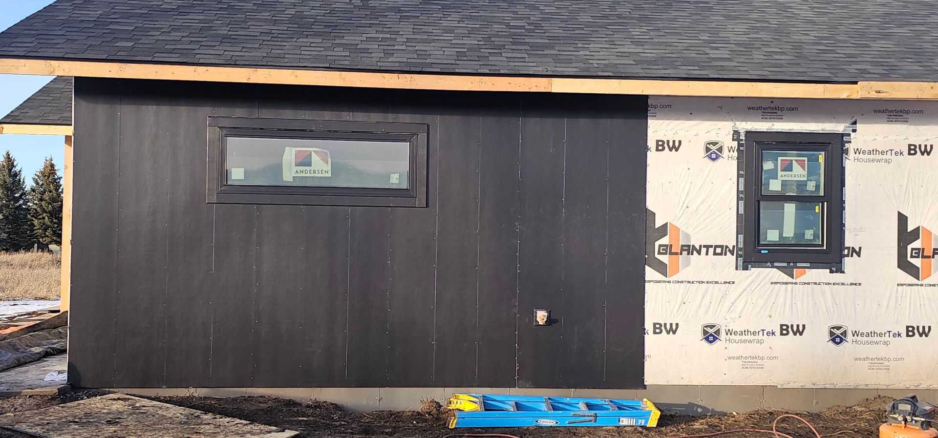 An unfinished house exterior featuring black vertical siding on the left and exposed white house wrap on the right.