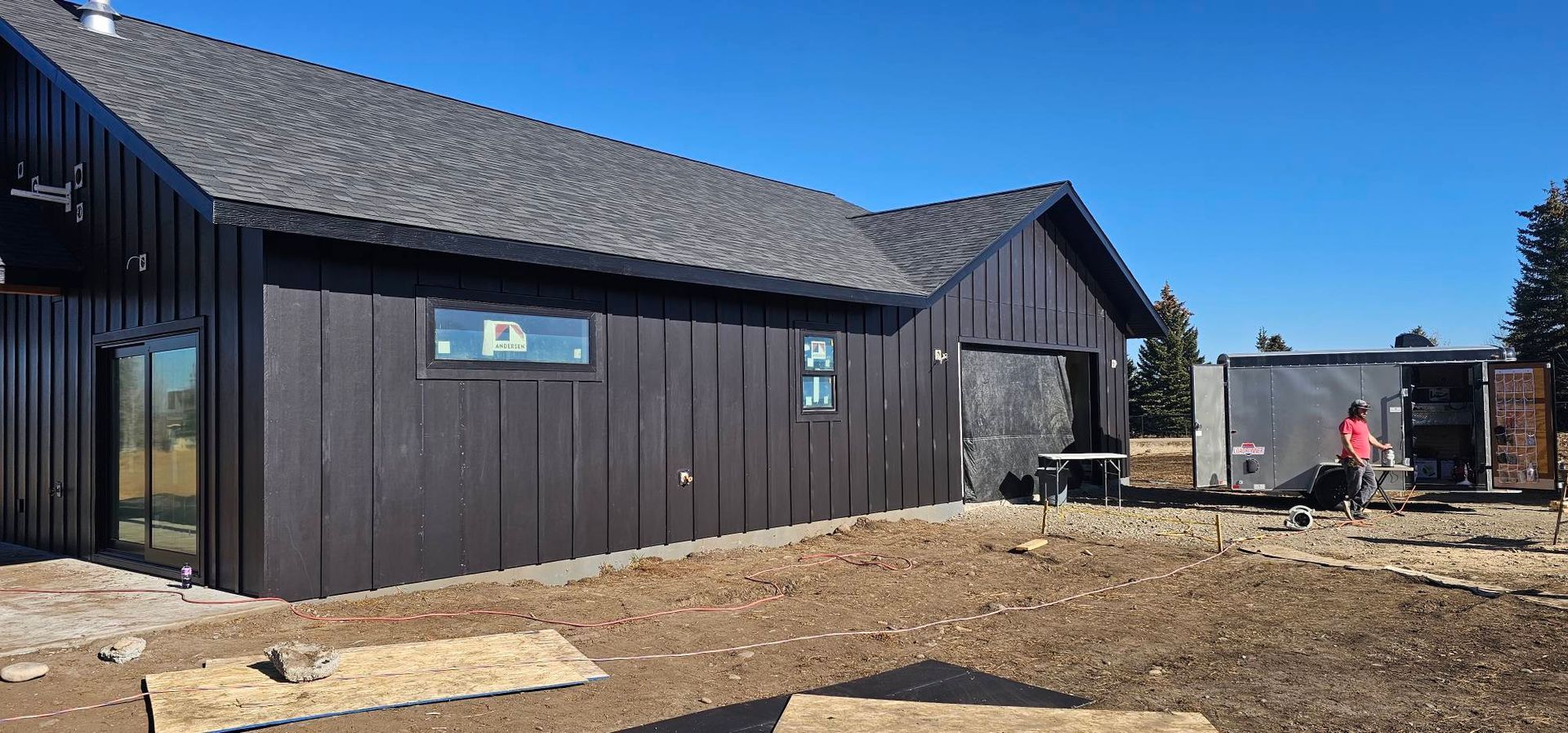 A modern black building with vertical siding under a clear blue sky, with a utility trailer parked on the side.