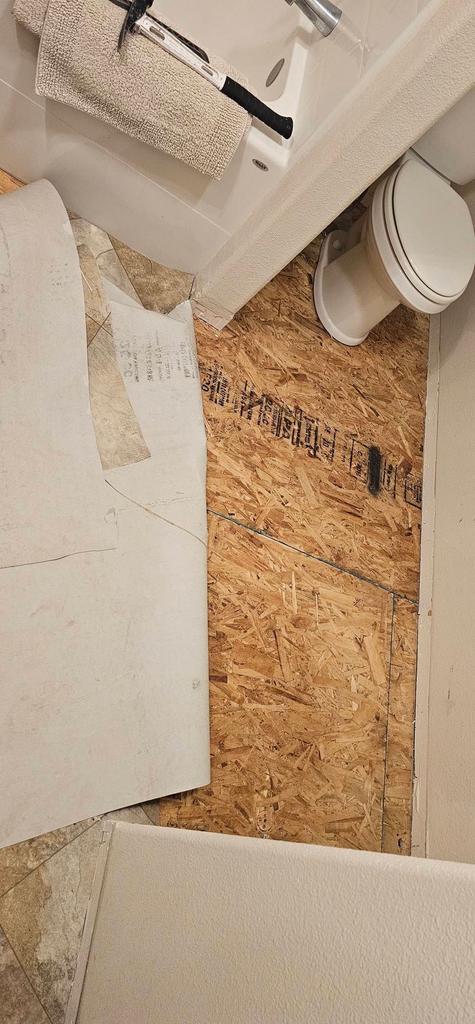 A bathroom under renovation with exposed wood subflooring, a white toilet, and a white bathtub.