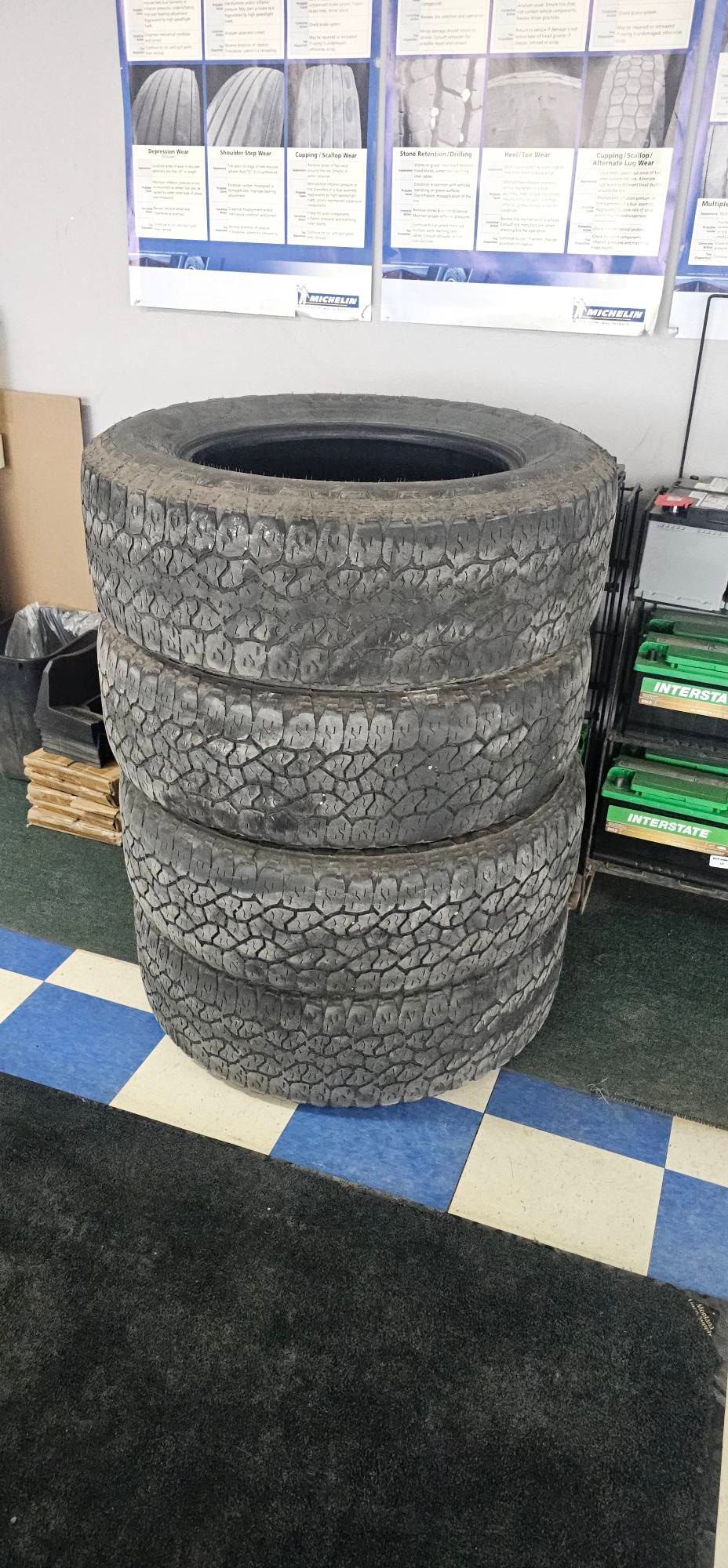 A stack of three used, all-terrain tires in a tire shop with informational posters on the wall.