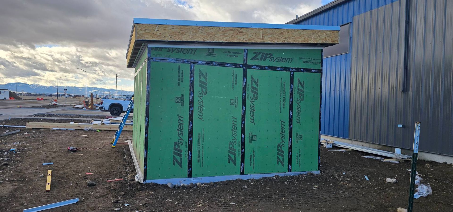 A small structure under construction with green ZIP System wall panels and a blue protective tape-covered roof.