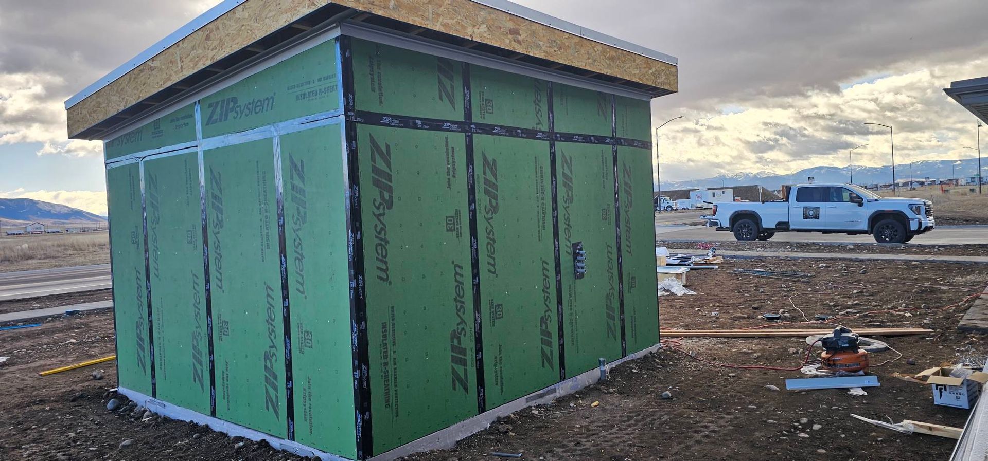 A small structure under construction with green ZIP System wall panels and taped seams in an open outdoor lot.