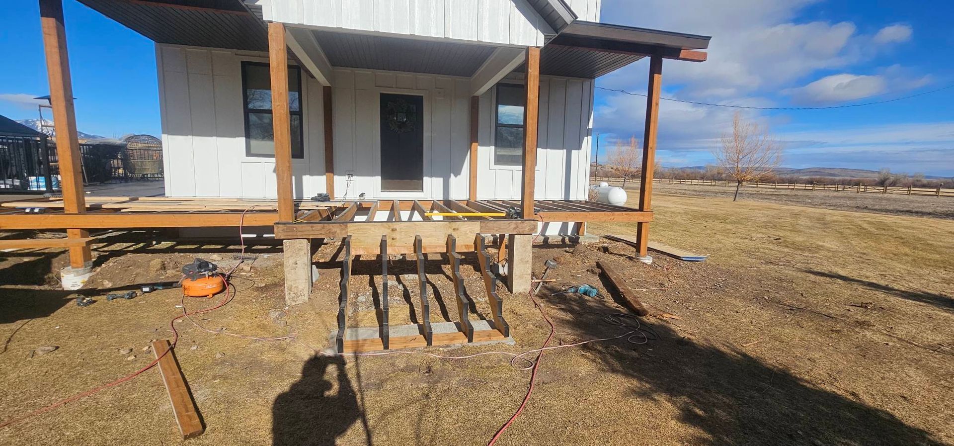 A wooden staircase frame being built for a house porch, with white exterior walls and a blue sky in the background.