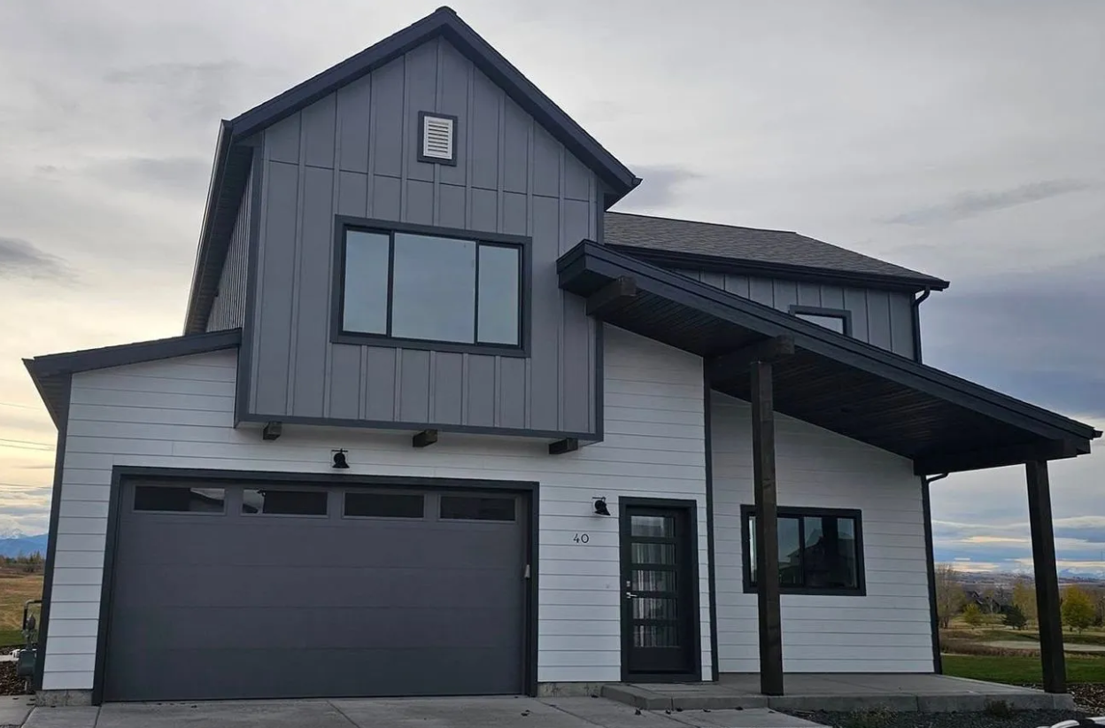 A modern two-story home with white horizontal siding on the lower level, grey vertical siding above, and a dark roof.