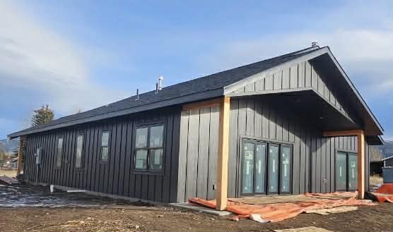A modern home under construction with dark vertical metal siding, a sloped roof, and light wooden support beams.