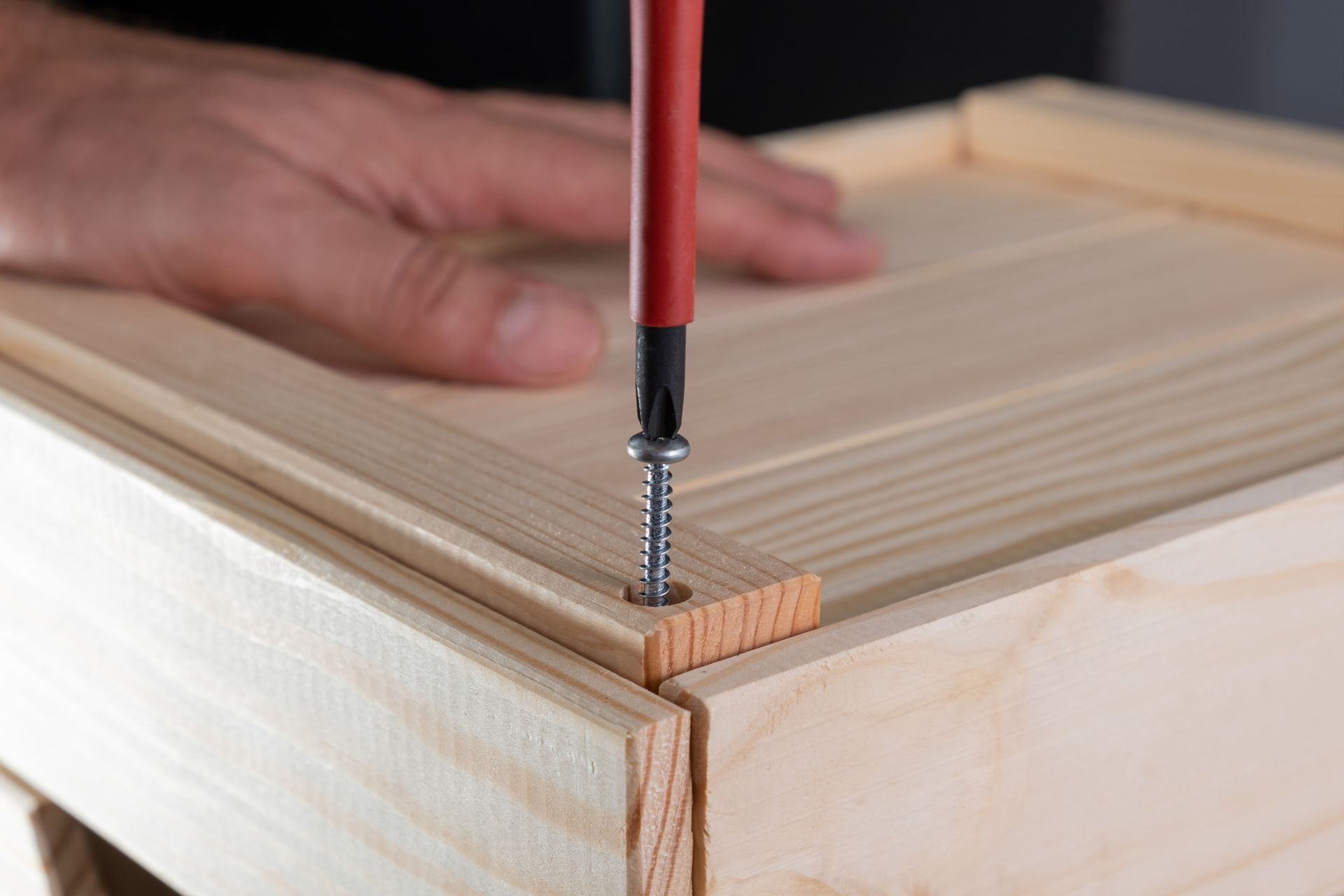 Persona che usa un cacciavite per avvitare una tavola di legno a una cornice di legno; primo piano.