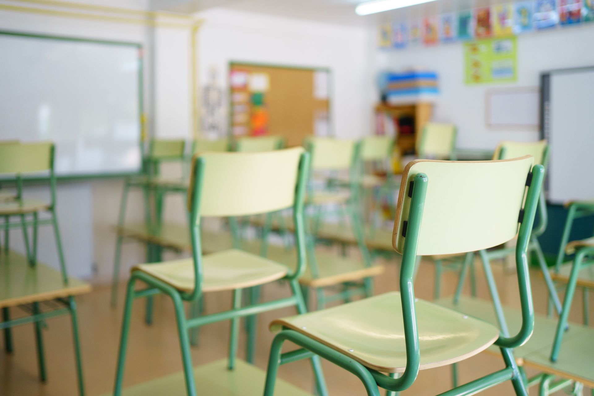 Aula vuota con file di sedie verdi di fronte a una lavagna.