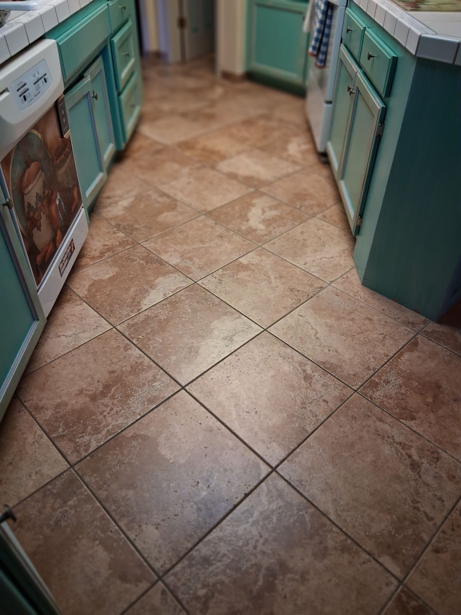 Brown tile floor in a kitchen with turquoise cabinets and a white stove.