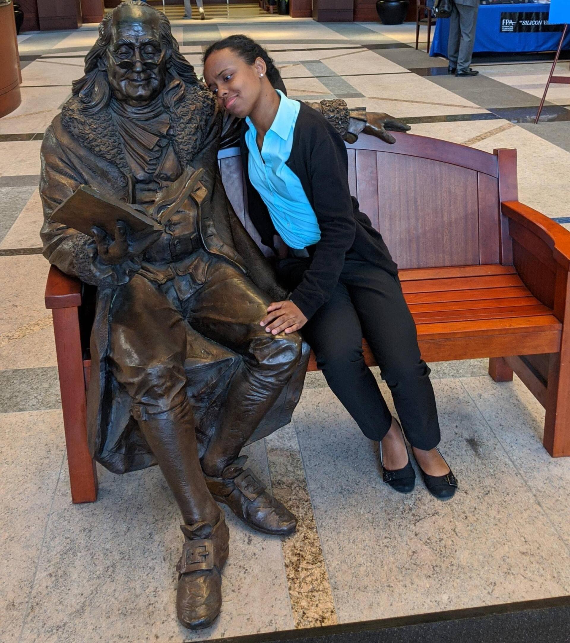 Bobbie sitting and looking over the shoulder a statue of Benjamin Franklin reading a book