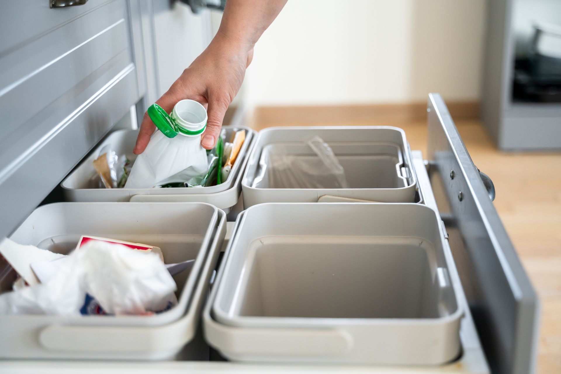 A person is putting a bottle of milk into a trash can in a kitchen.