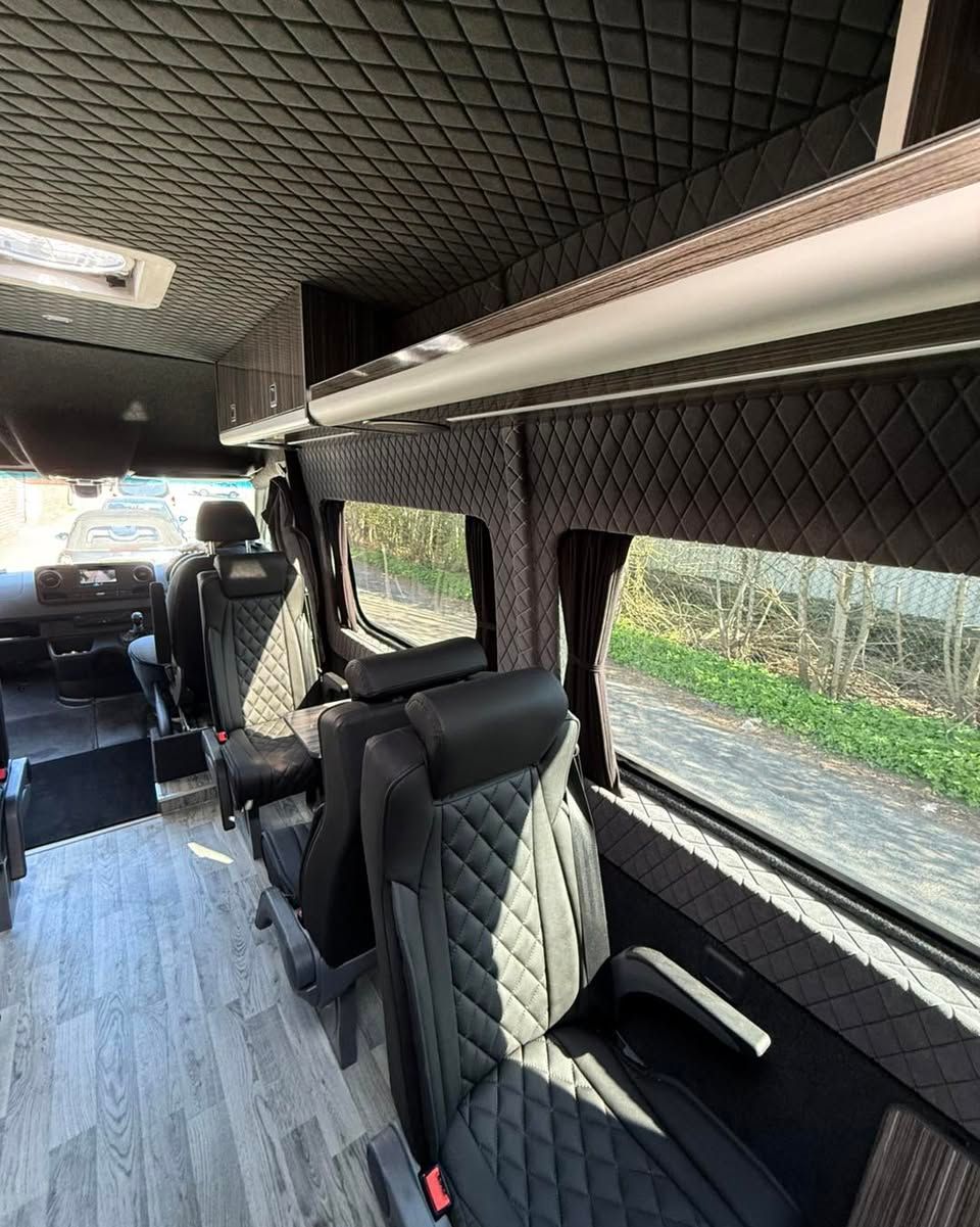 Interior of a black quilted golf passenger van with rows of scotseat seats and sunlight through the windows.