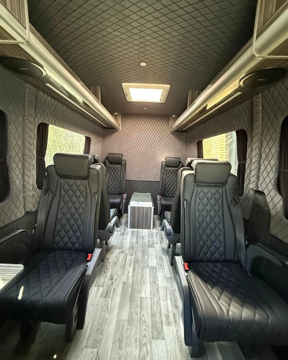 Luxurious van interior with scotseat black quilted seats and a light wood-look floor, viewed from the rear toward the front.