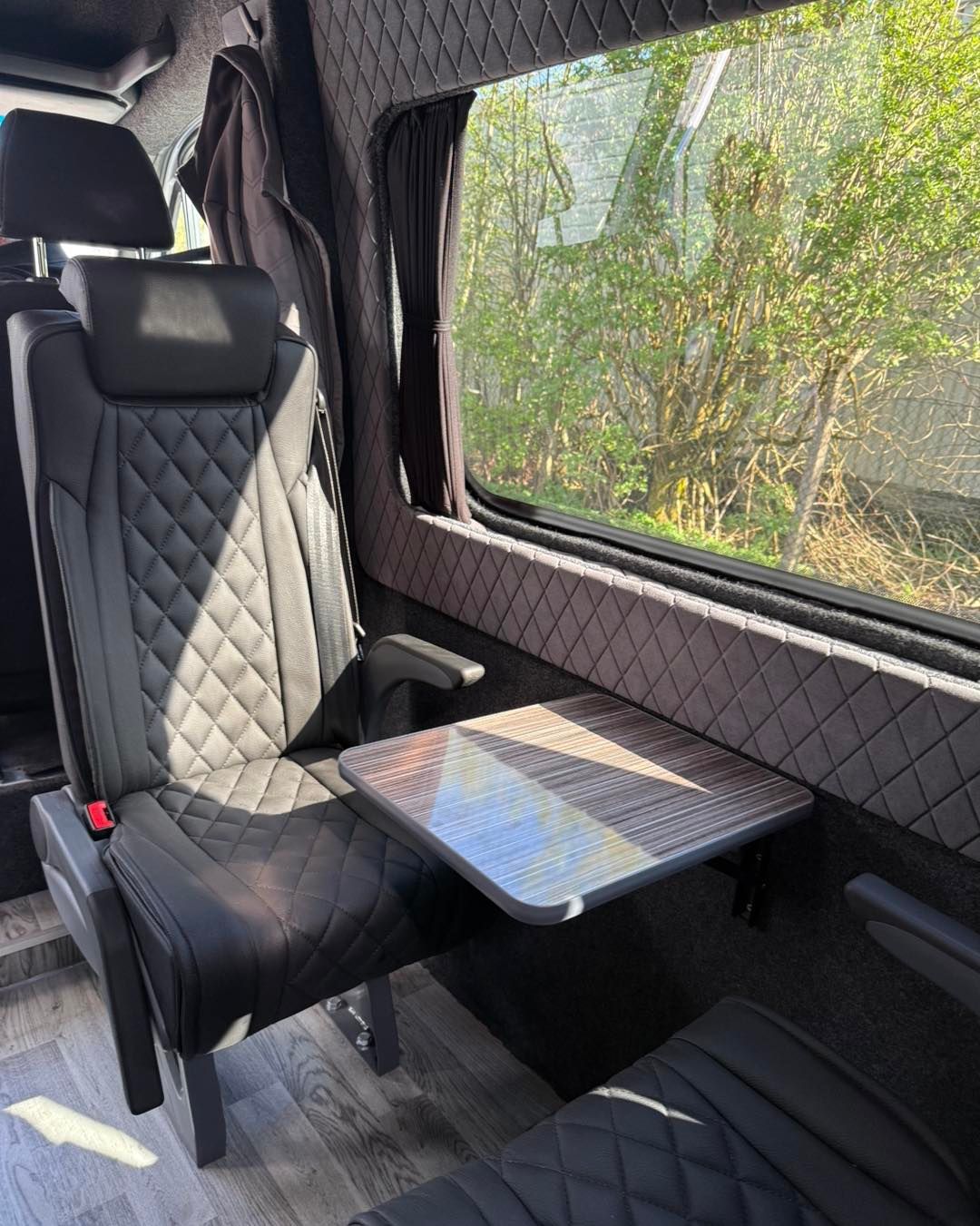 a close up of a scotseat seat with a small table by a window, showing quilted black upholstery and sunlight outside