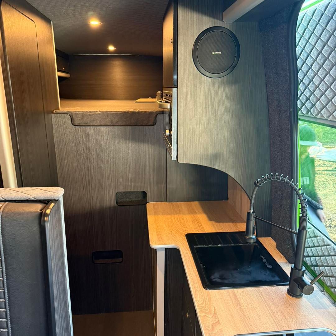Compact kitchenette with wood cabinets, black sink, and a small window.