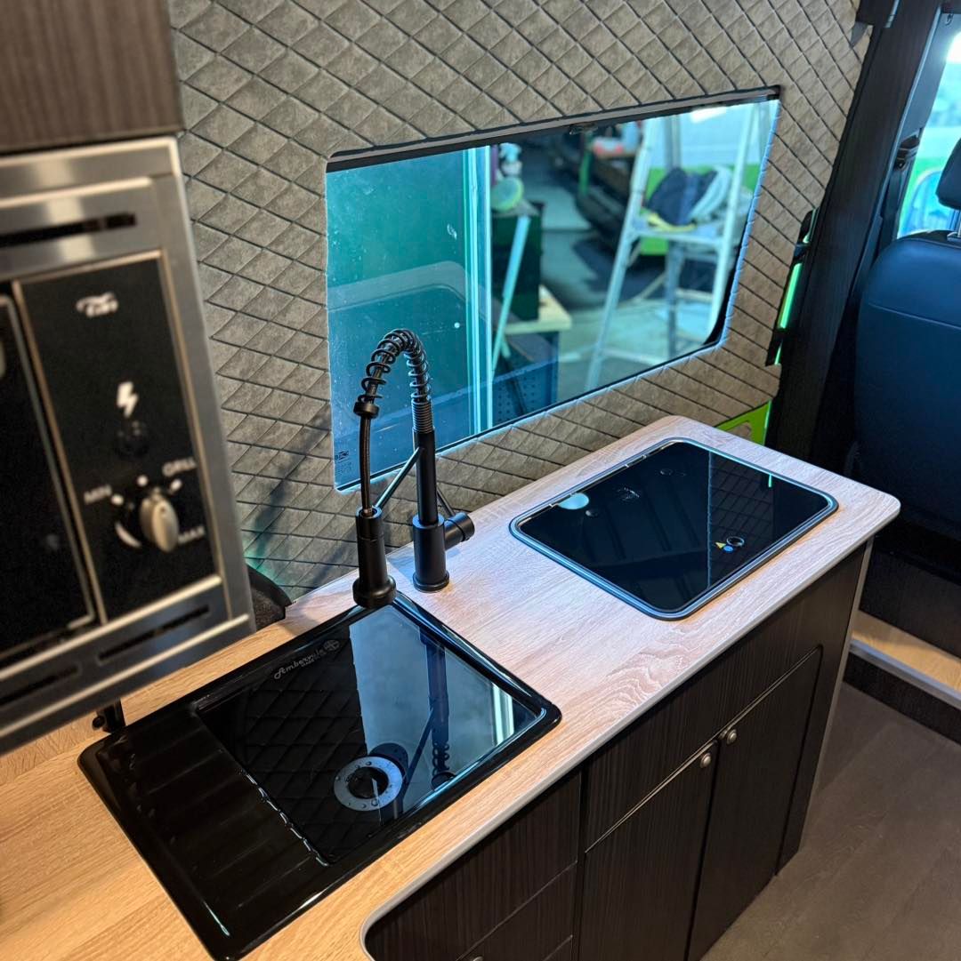 Compact RV kitchenette with black sink, small cooktop, and mirrored backsplash in a modern interior