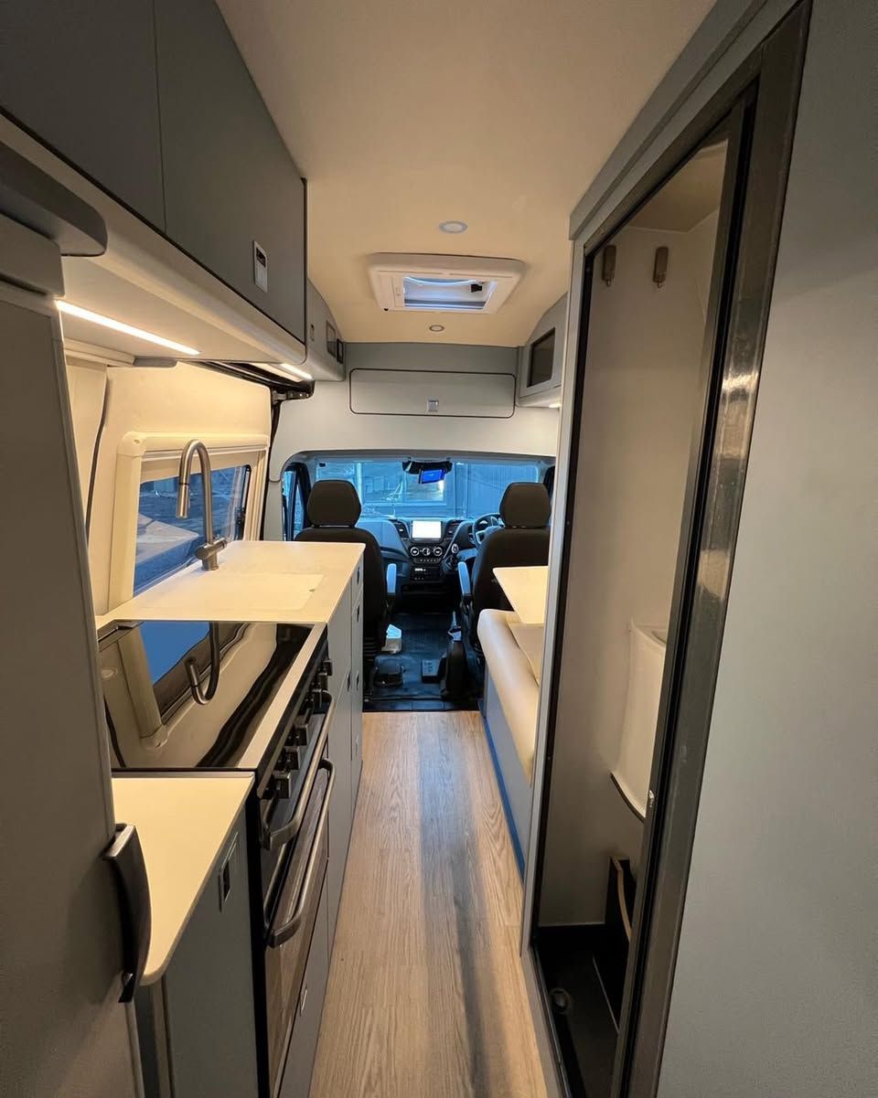 modern camper van interior with kitchenette, overhead storage, and front cab seats visible.