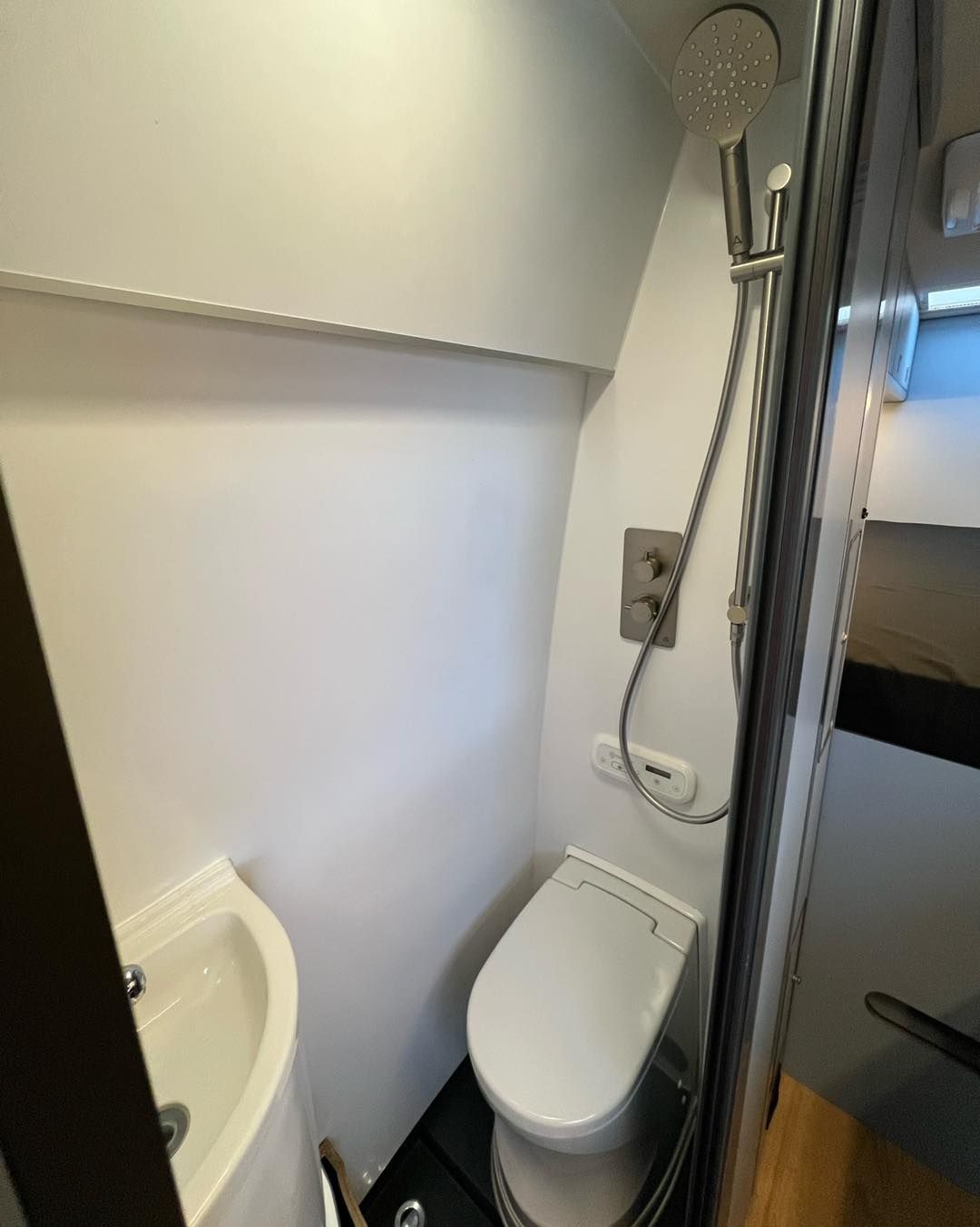 bathroom with a toilet, sink, shower door, and wall-mounted controls.