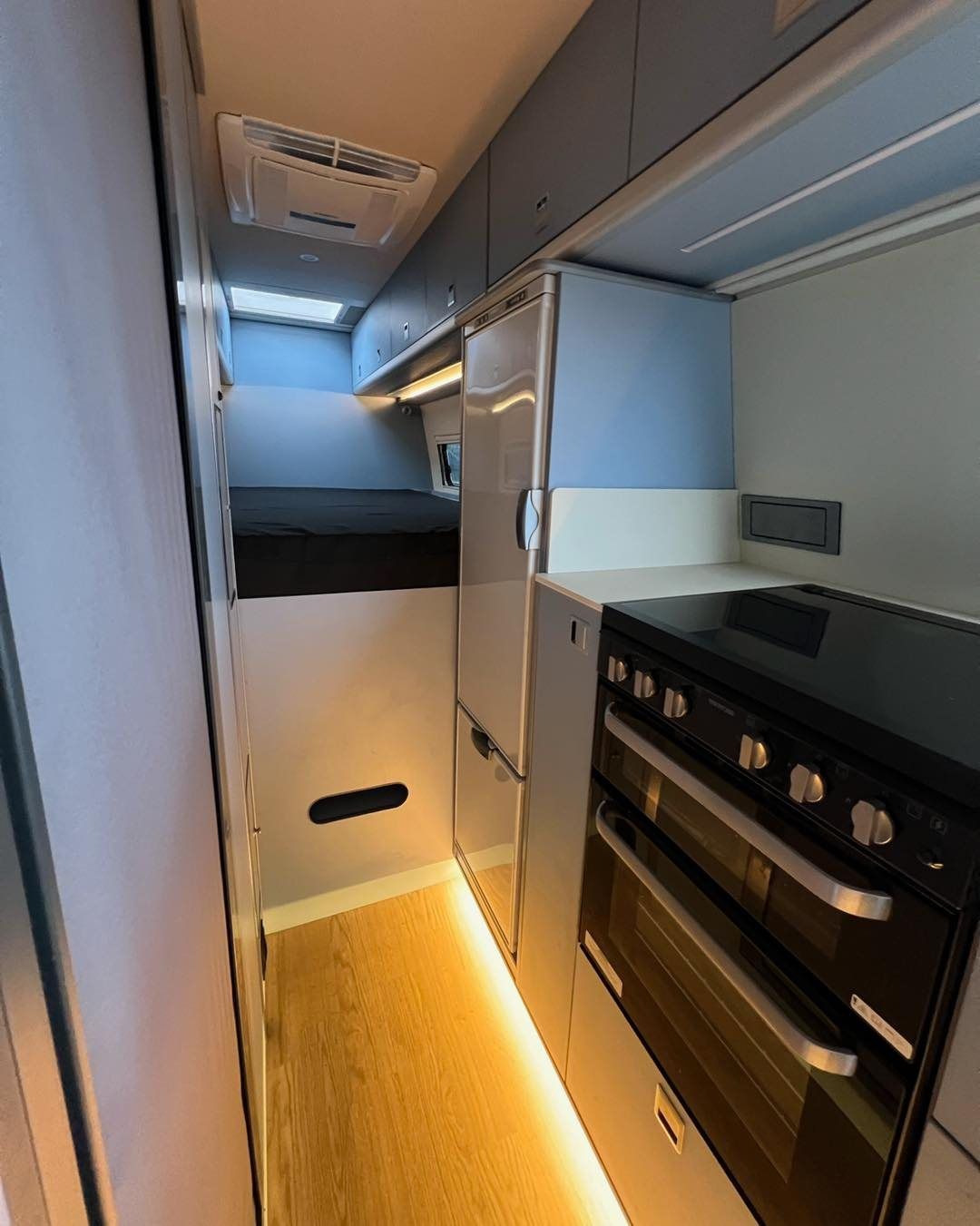 interior showing a black stove, sink, light wood floor, and sleeping area ahead