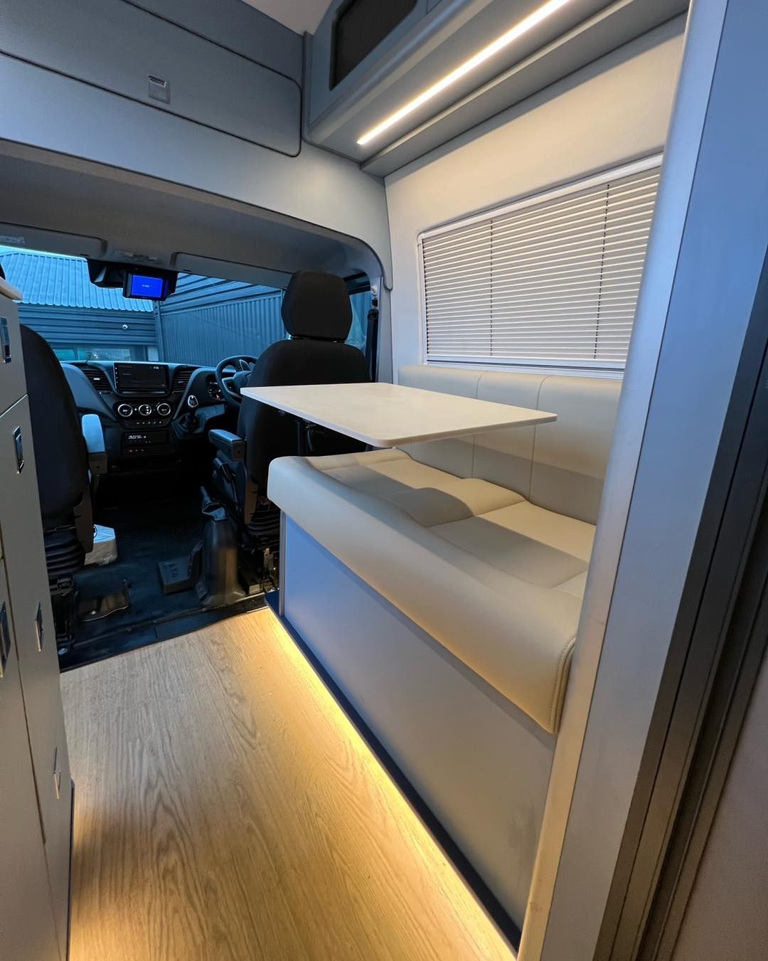 Compact camper van interior with fold-out table, bench seating, and LED lighting