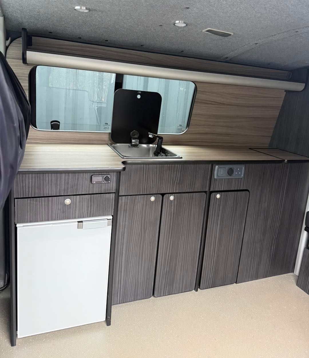 Compact camper kitchen with sink, cabinets, countertop, mirror, and mini fridge in gray wood finish