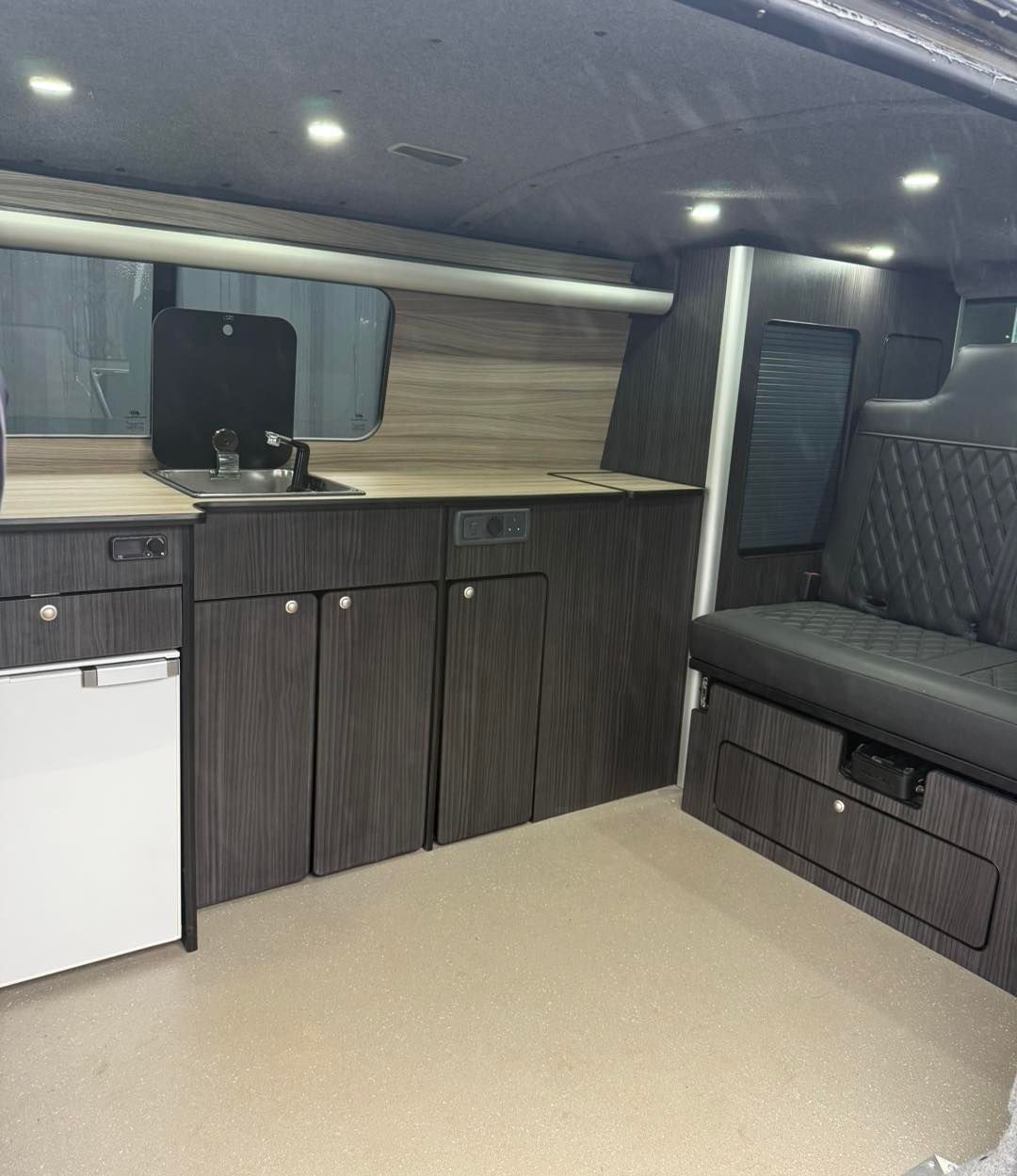 Compact camper van interior with kitchenette, sink, storage cabinets, and gray bench seating