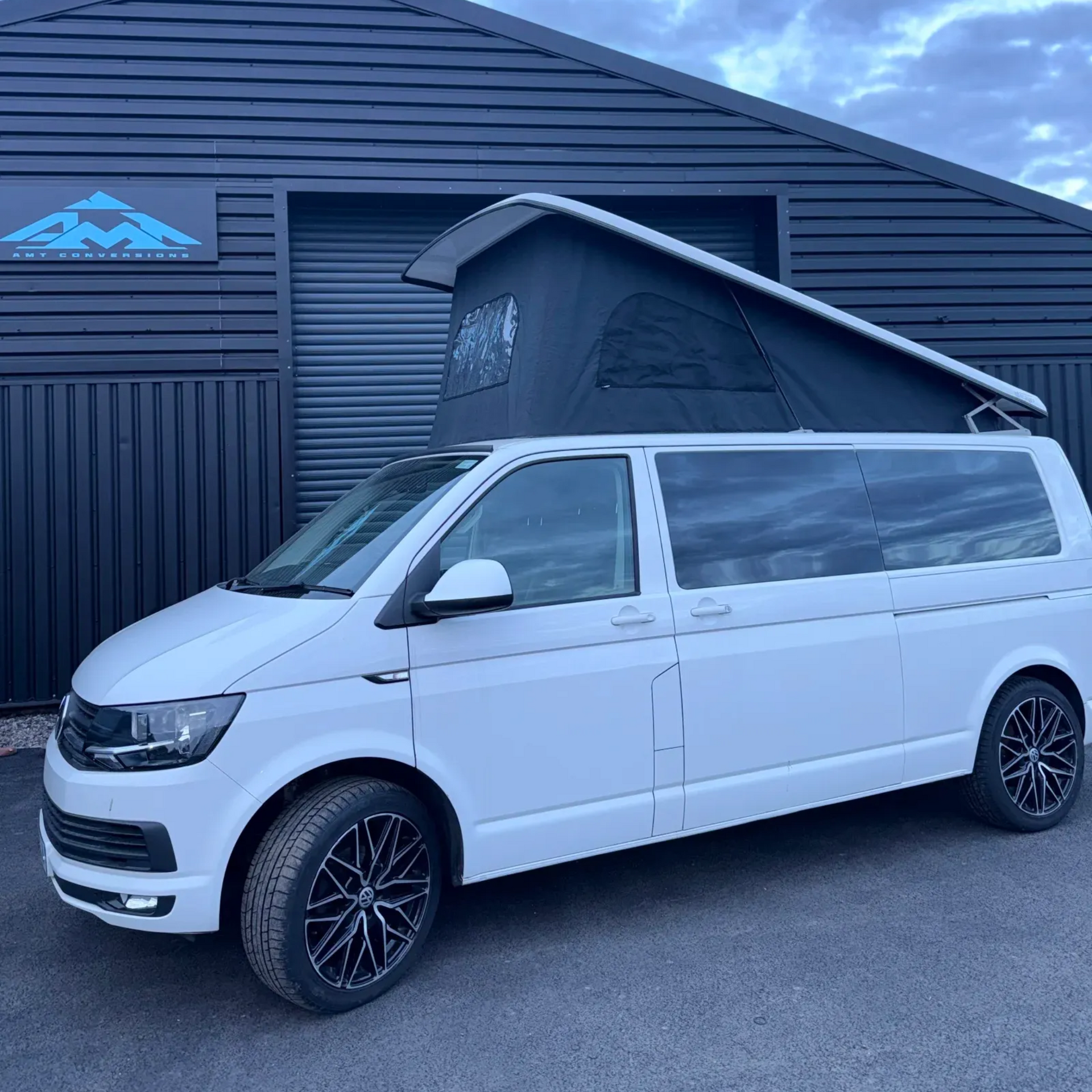 White camper van with raised pop-top roof parked outside a dark building