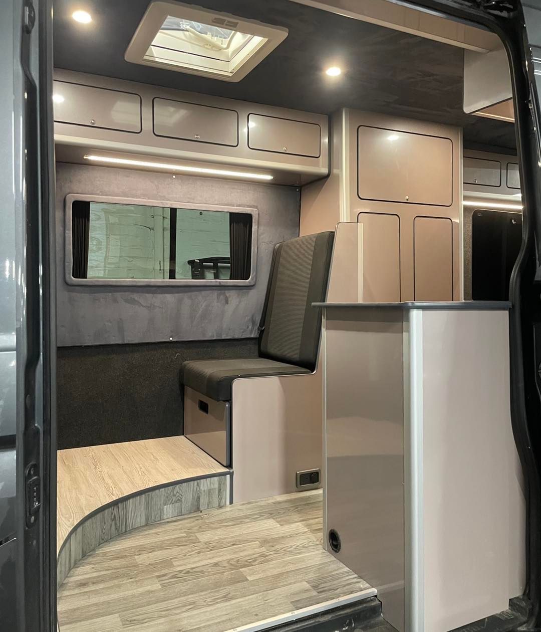 Modern camper van interior with wood cabinetry, bench seating, and a skylight