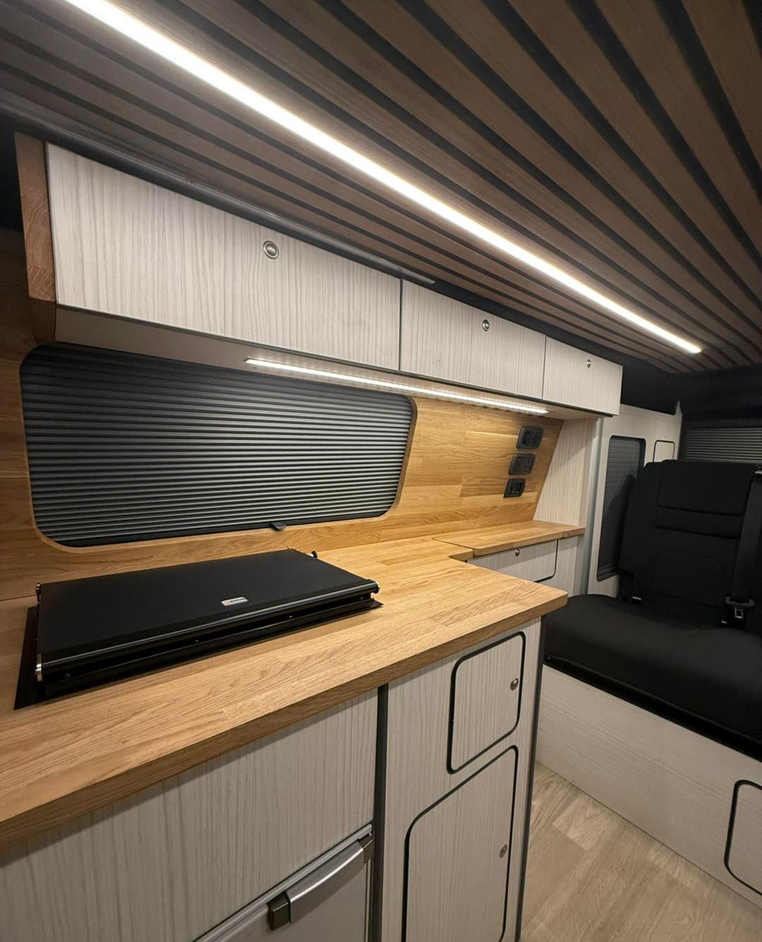 modern camper van interior with wooden countertop, black sink cover, white cabinets, and bench seat