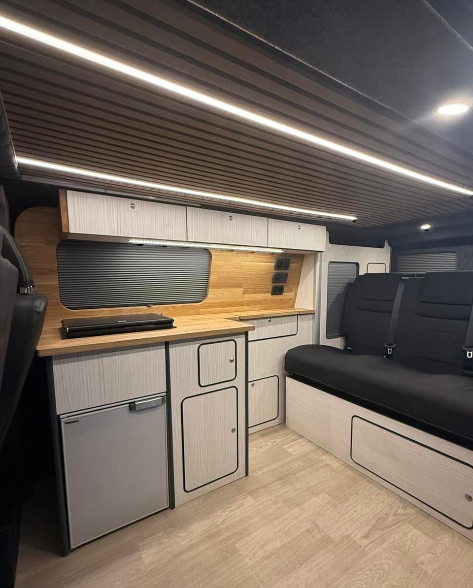 camper van interior with kitchenette, storage cabinets, and black rocknroll bed under LED strip lights