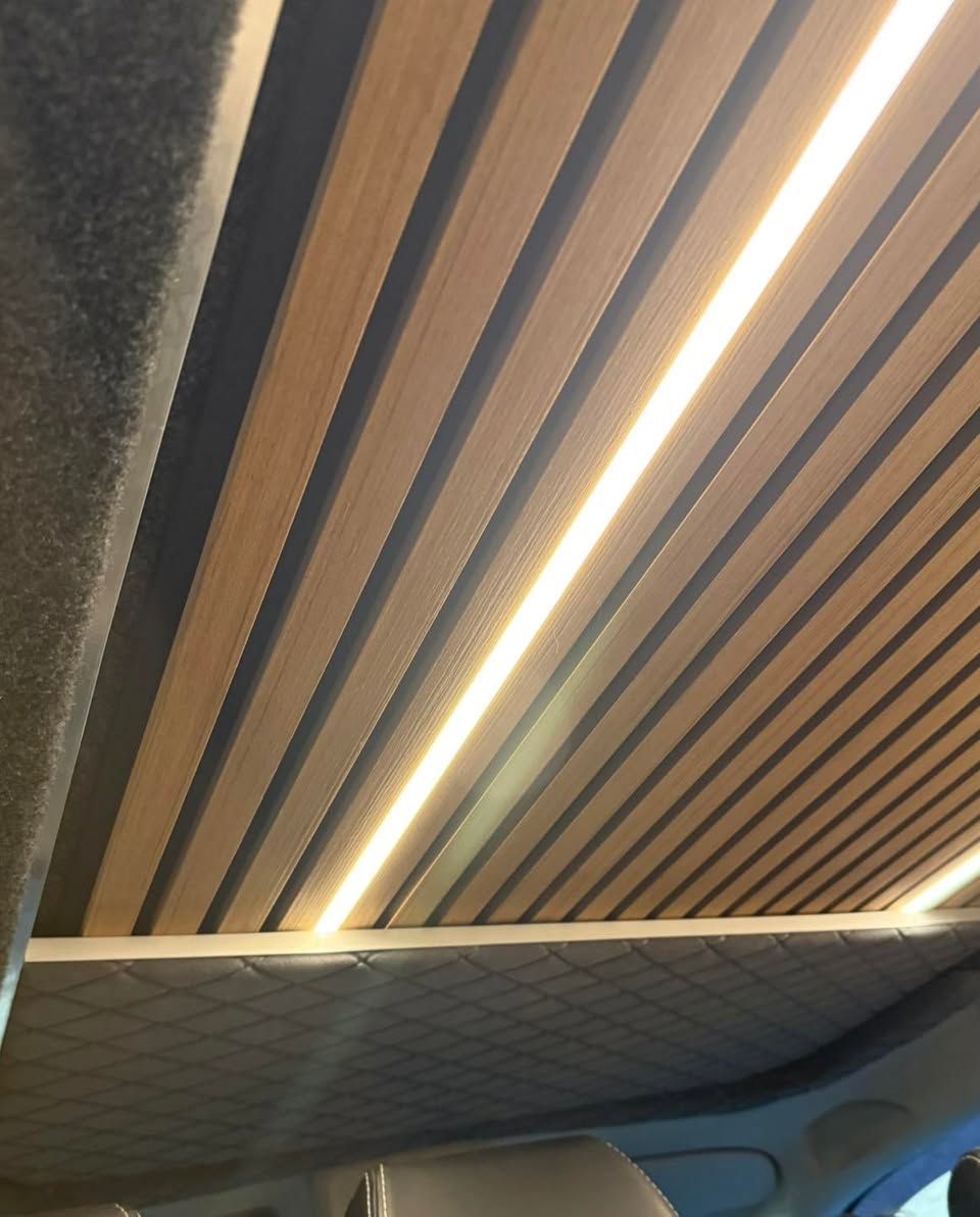Ceiling with wooden slats and a long warm LED strip light in an interior space