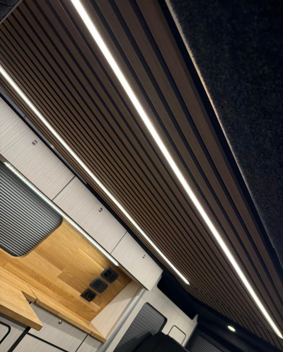 Modern campervan interior with wood slat ceiling, long lights, and a worktable with chairs