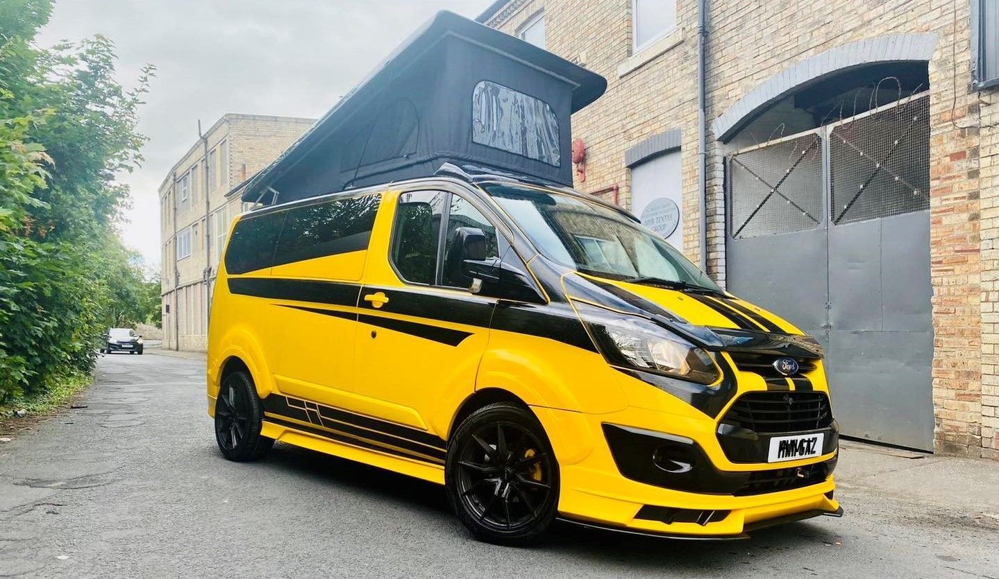 Bright yellow customized van with black accents parked on a city street, side canopy raised open