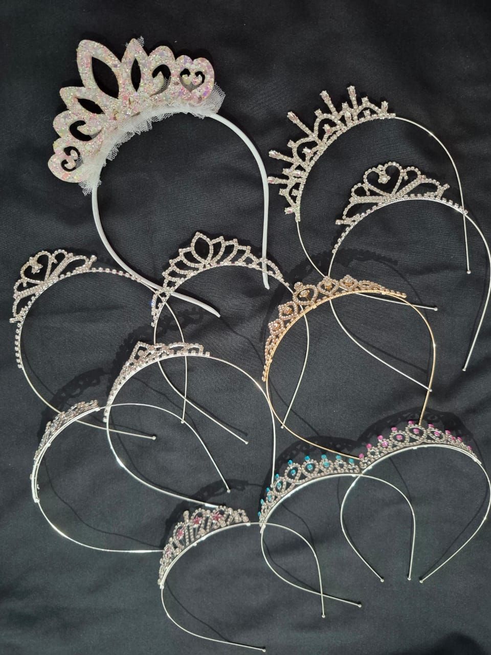 Tiaras y diademas de alambre dorado superpuestas dispuestas sobre tela oscura.