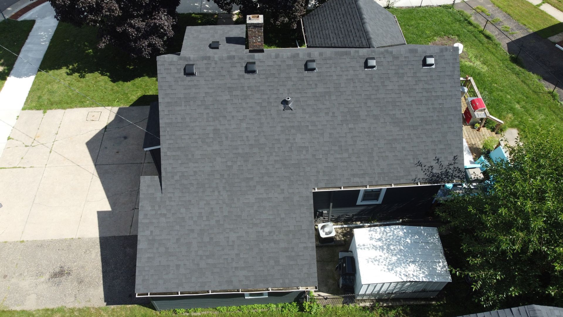 Overhead view of a house with a dark gray shingle roof, chimney, and adjacent patio.