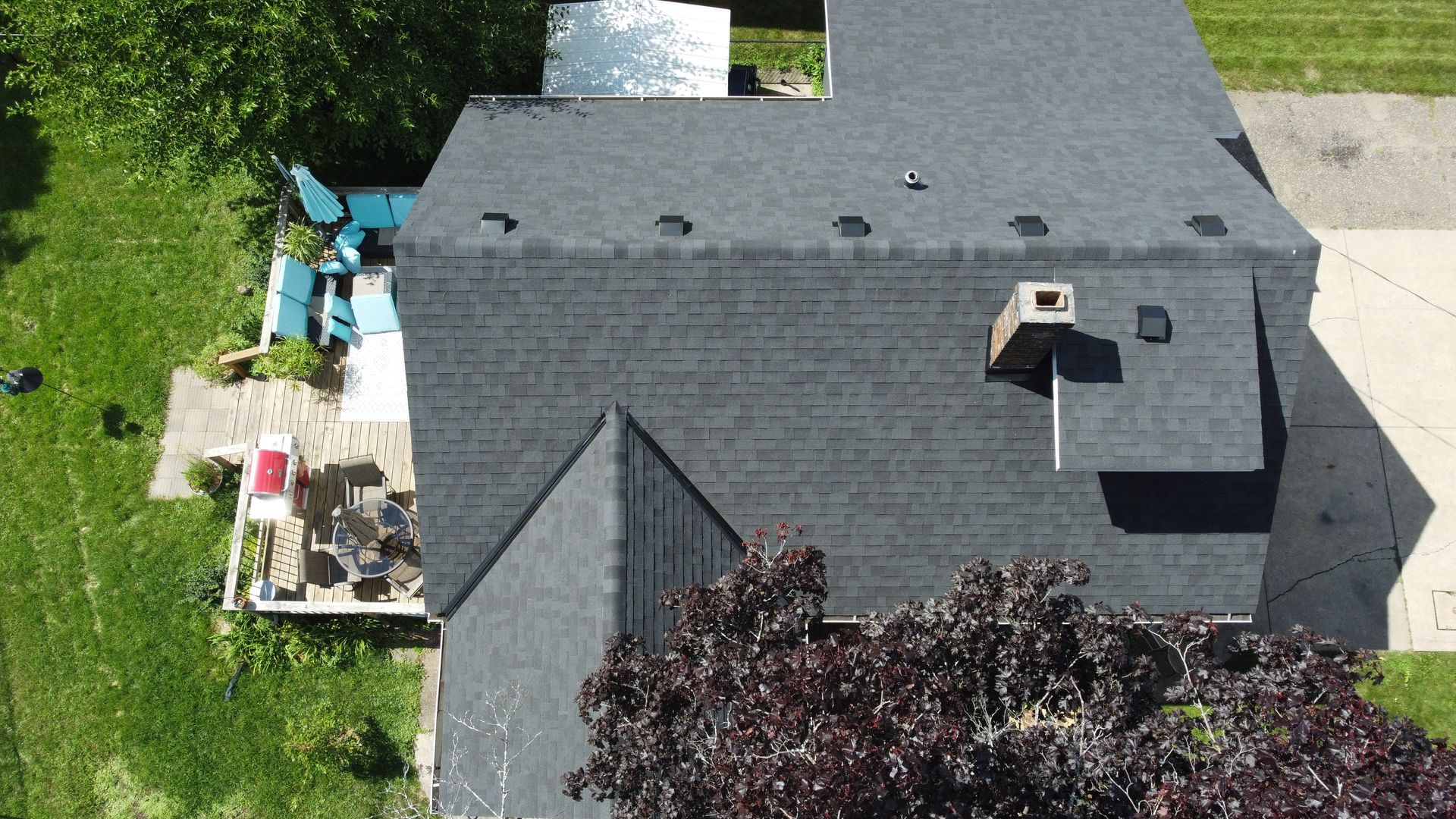 Overhead view of a house with a dark gray shingled roof, chimney, and surrounding green lawn.