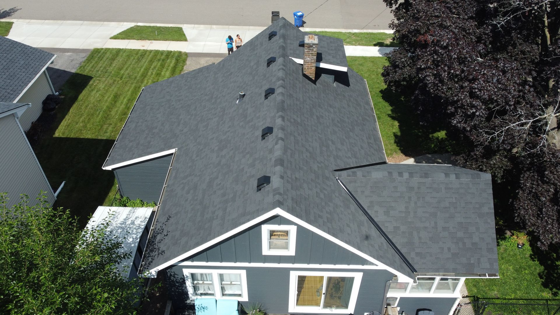 Aerial view of a dark grey house with a matching roof, surrounded by green lawn and trees.