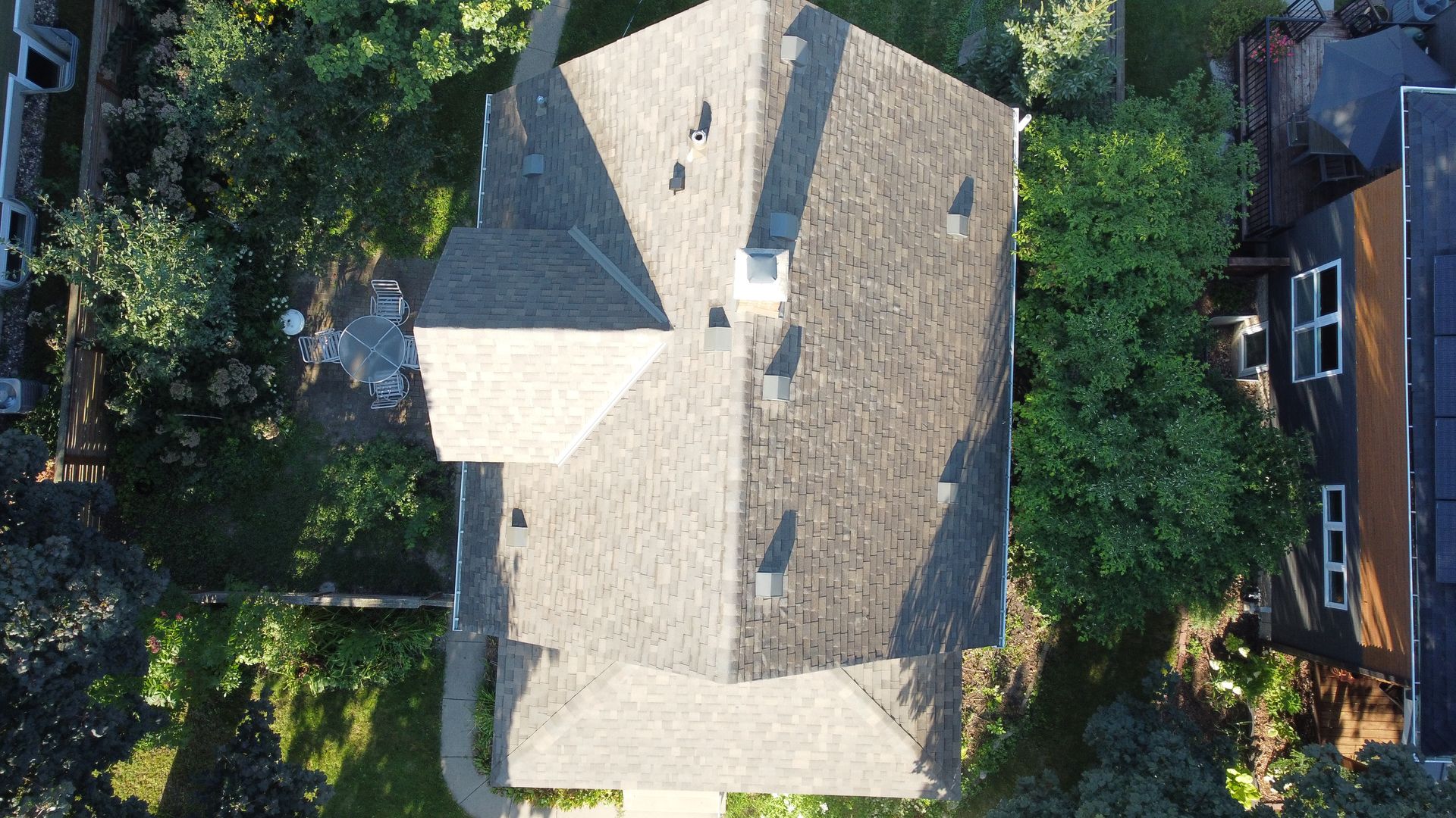 Overhead view of a house with a gray roof, chimneys, and surrounding trees.
