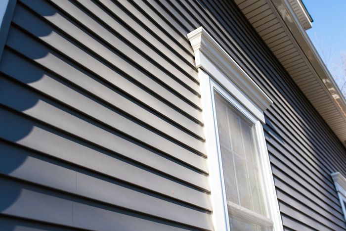Gray horizontal siding on a house, white trim around a window, blue sky. Gray horizontal siding on a house, white trim around a window, blue sky.