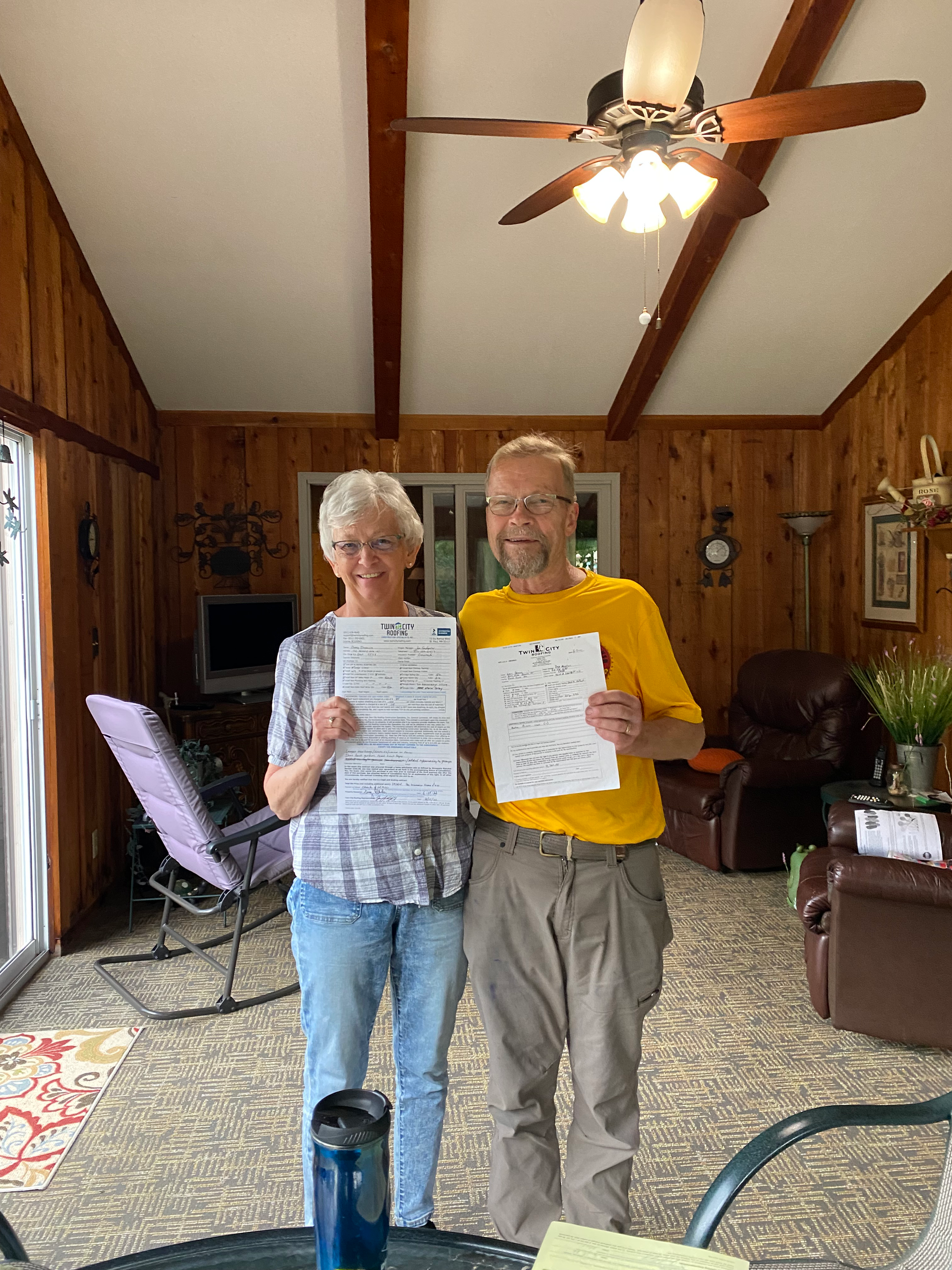 A man and a woman are standing in a living room holding papers.