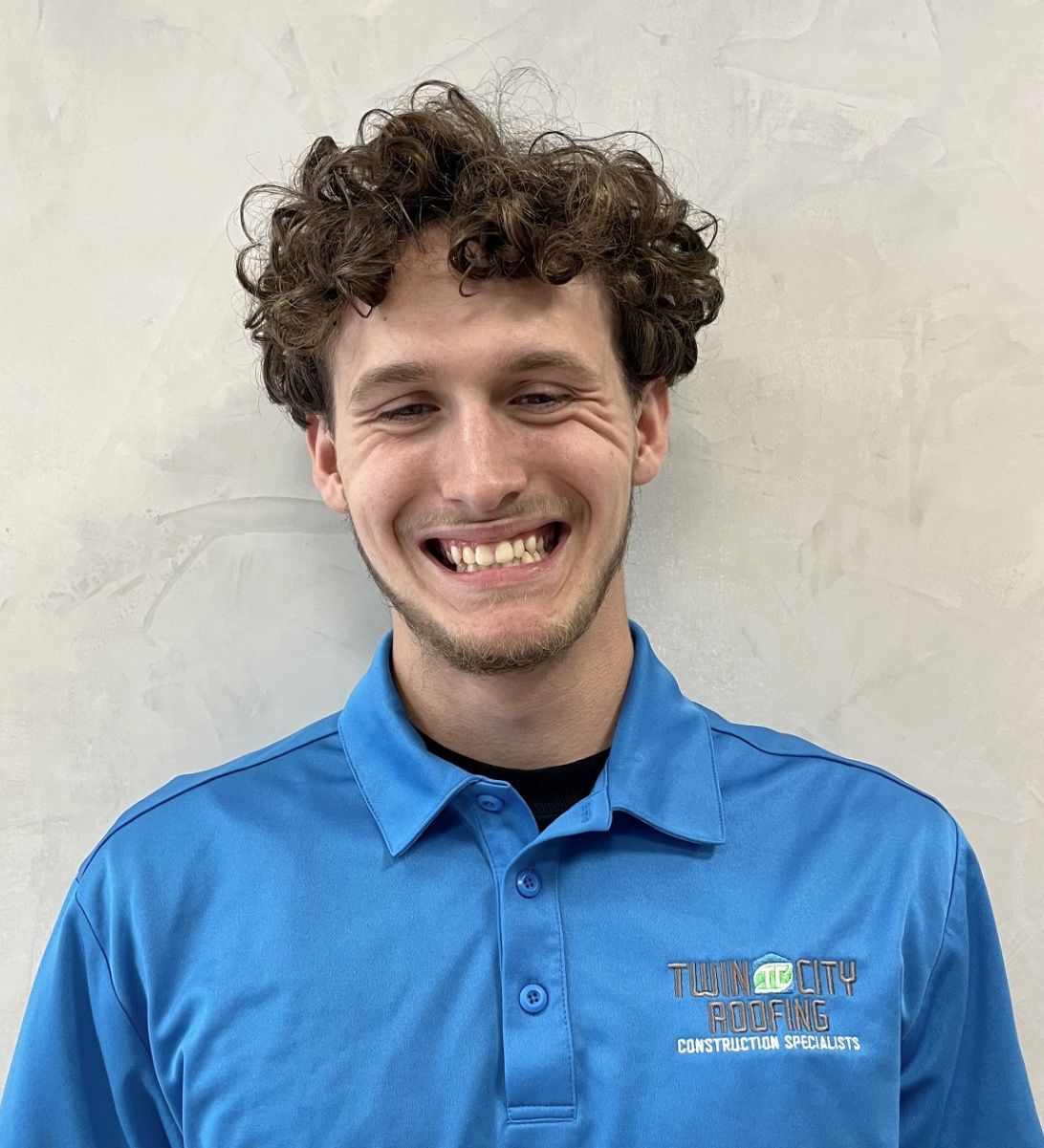 Man with curly hair smiling, wearing a blue polo shirt. Light background.