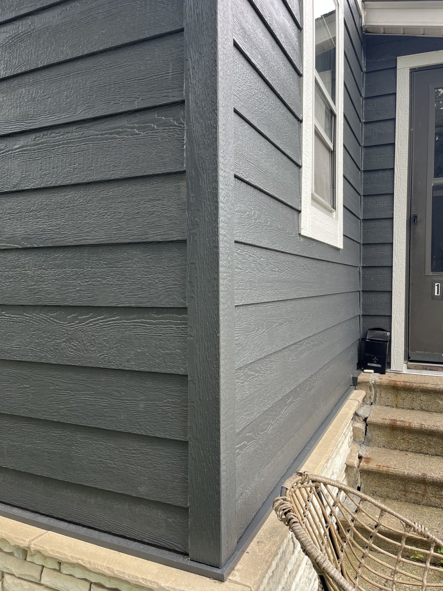 Dark gray siding on a house corner. A window and door are visible. Exterior view.